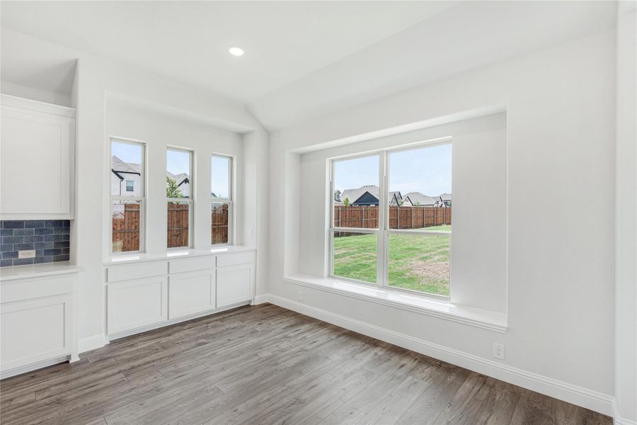 Bright dining area with hardwood floors, large windows, and white wainscoting overlooking a backyard