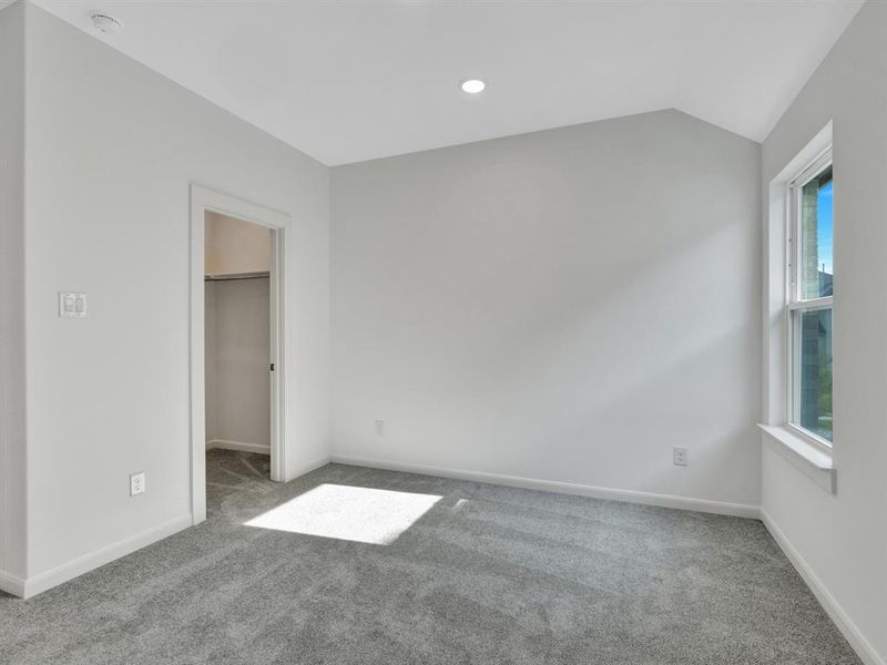 Unfurnished bedroom featuring a closet, a spacious closet, carpet, and vaulted ceiling