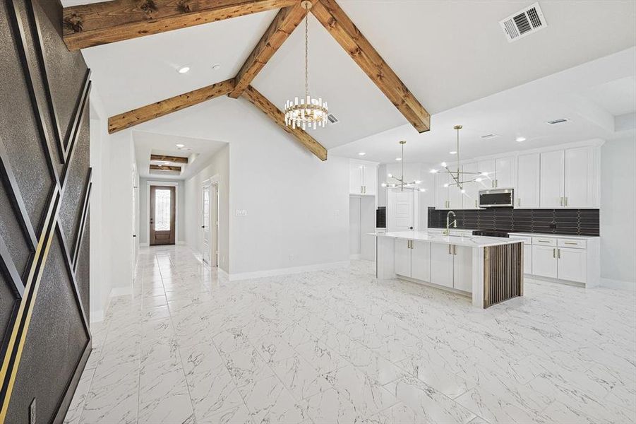 Kitchen with pendant lighting, white cabinetry, backsplash, a kitchen island with sink, and an inviting chandelier