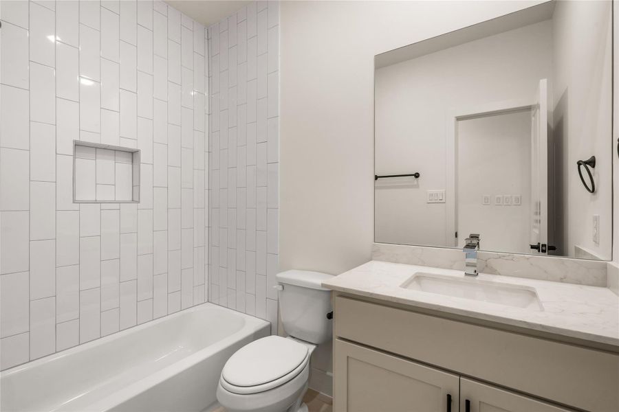 Secondary bath — designer white vertical stack tile surround, inset storage niche, deep soaking tub, and quartz-topped vanity.