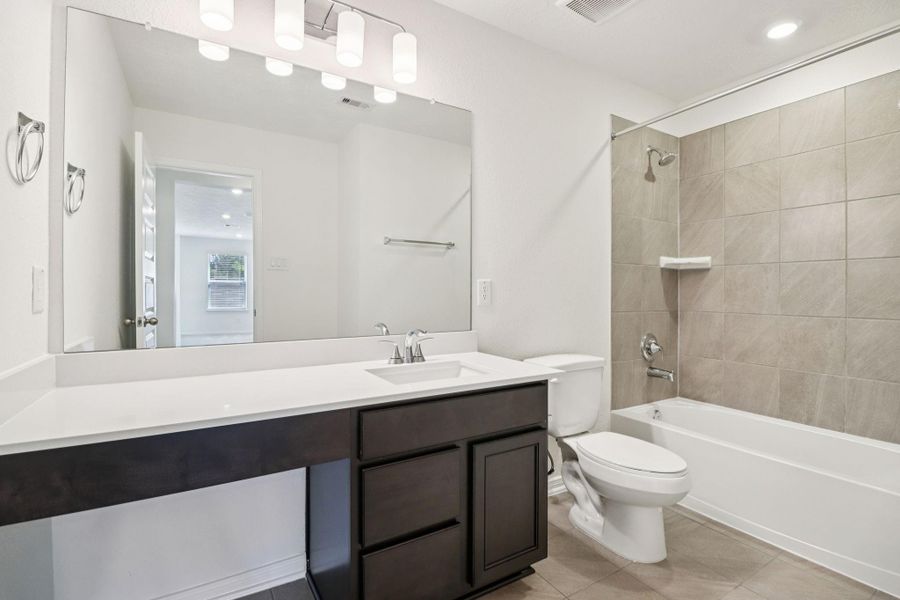 The secondary bathroom showcases tile flooring, a bath/shower combo with tile surround, a vanity with knee space and stunning light countertop, a mirror, sleek fixtures, and contemporary finishes throughout.