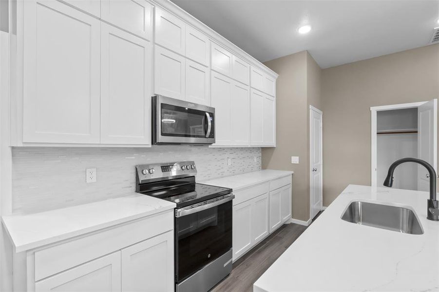 Kitchen with sink, appliances with stainless steel finishes, white cabinetry, light stone counters, and tasteful backsplash