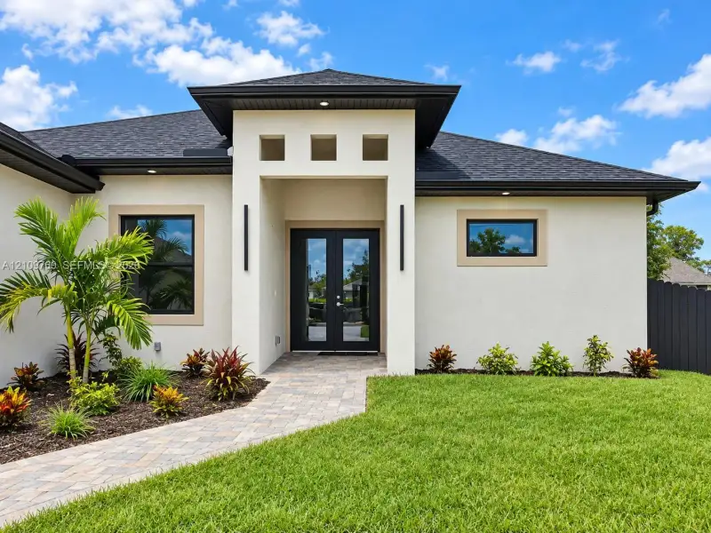 Modern stucco exterior featuring double glass entry doors, a multi-tiered roofline, square clerestory windows, and a paved stone walkway
