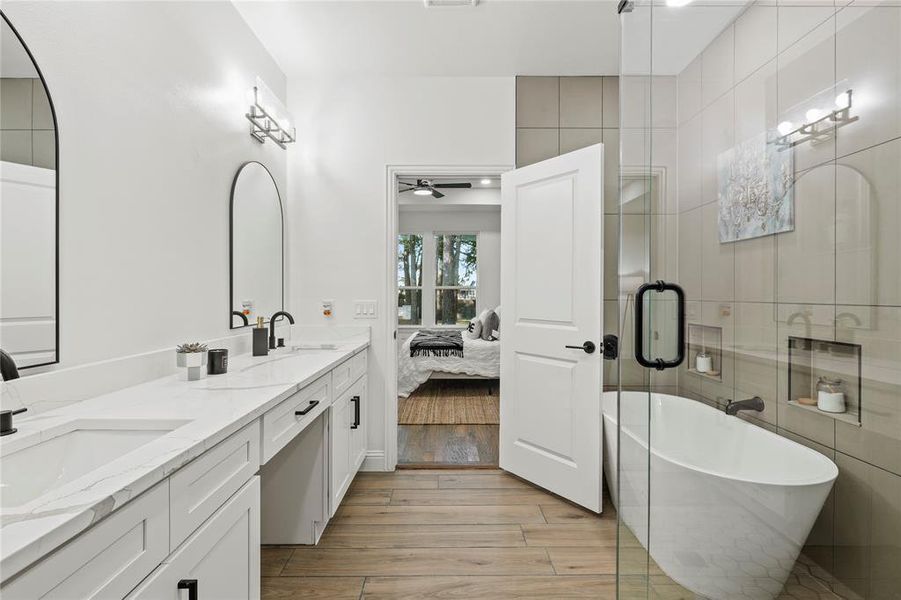 Ensuite bathroom featuring double vanity, a freestanding tub, ceiling fan, light wood-style floors, and a shower with shower door