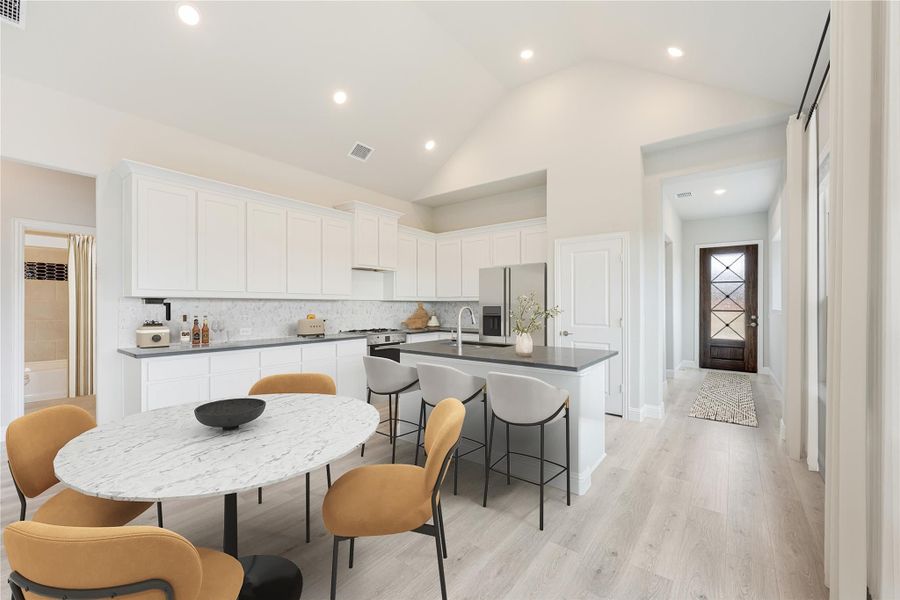 Open kitchen and dining area with white cabinets, center island, marble dining table, and light wood floors