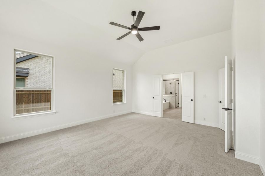 Empty master bedroom with vaulted ceiling, ceiling fan, carpet floors, and ensuite bathroom doorway Empty master bedroom with vaulted ceiling, ceiling fan, carpet floors, and ensuite bathroom doorway