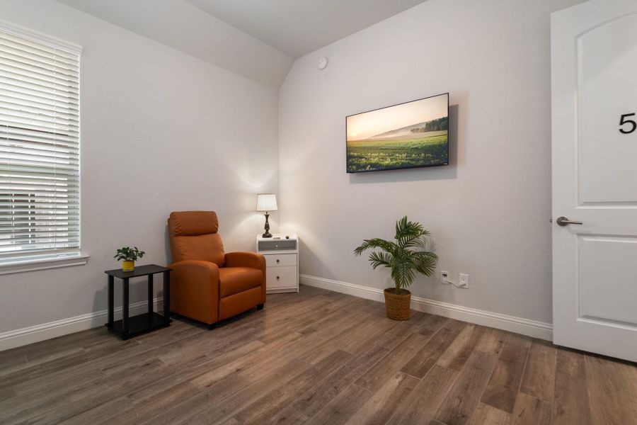 This cozy room features a comfortable armchair, side tables with plants, and a wall-mounted landscape artwork. It has warm wood flooring, soft lighting from a table lamp, and ample natural light from a window with blinds. Perfect for relaxation or reading. This cozy room features a comfortable armchair, side tables with plants, and a wall-mounted landscape artwork. It has warm wood flooring, soft lighting from a table lamp, and ample natural light from a window with blinds. Perfect for relaxation or reading.