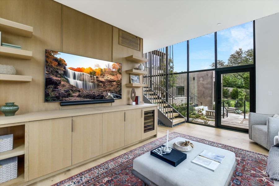 Open-concept living space with full-height glazing, wood-finish flooring, and a built-in media center with integrated shelving