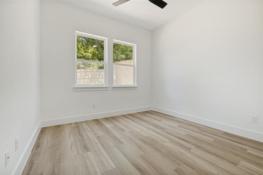 Room featuring wood-finish flooring, white baseboards, and two windows Room featuring wood-finish flooring, white baseboards, and two windows