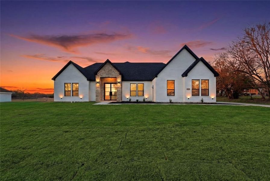 Back of property at dusk featuring stone siding and a yard