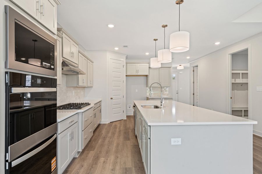 Kitchen featuring stainless steel appliances, light wood-type flooring, an island with sink, light stone counters, and backsplash