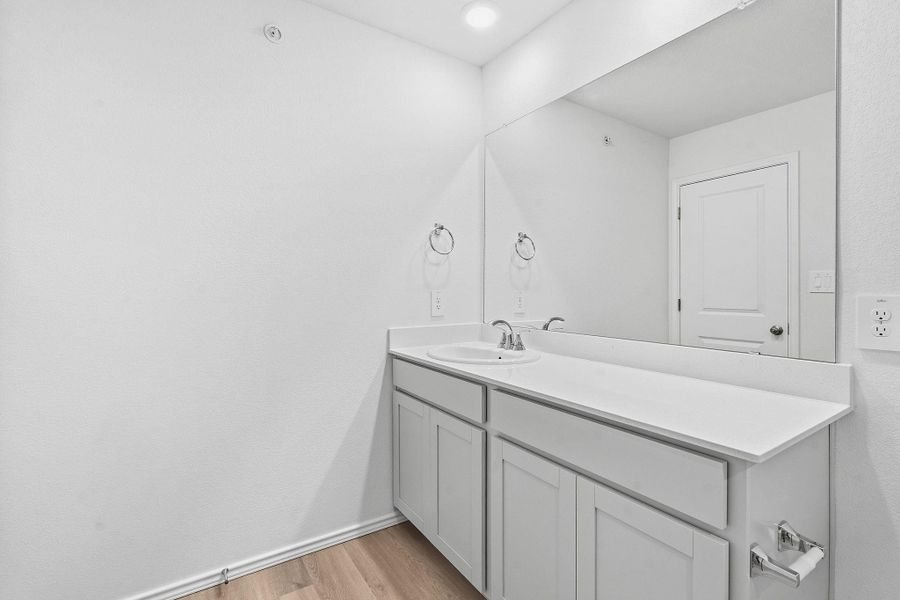 Bathroom vanity featuring light-toned cabinetry, an integrated sink, and a large wall-mounted mirror Bathroom vanity featuring light-toned cabinetry, an integrated sink, and a large wall-mounted mirror