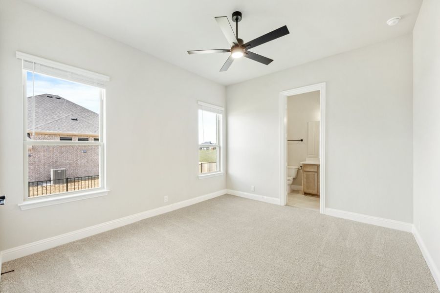 Bedroom with carpet flooring, ceiling fan, two windows, and an attached ensuite bathroom visible through open doorway. Bedroom with carpet flooring, ceiling fan, two windows, and an attached ensuite bathroom visible through open doorway.