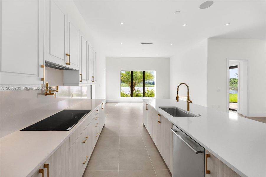 Modern kitchen with white cabinetry, gold-finish hardware, built-in cooktop, and an integrated dishwasher