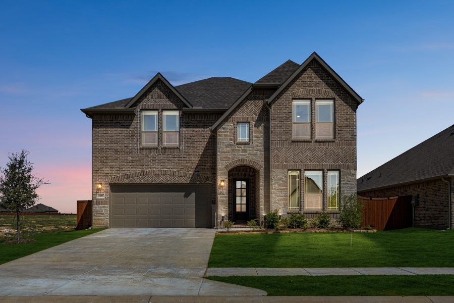 Two-story brick home with arched entry, two-car garage, and manicured front lawn at dusk Two-story brick home with arched entry, two-car garage, and manicured front lawn at dusk