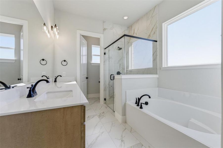 Full bathroom featuring a bath, double vanity, a marble finish shower, light marble finish floors, and recessed lighting