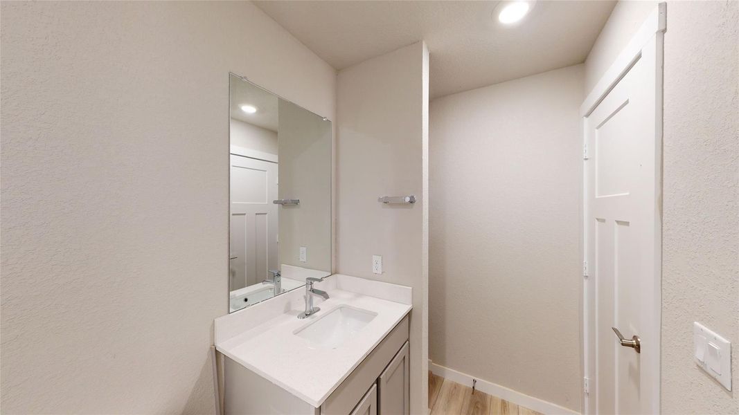 Half bathroom with vanity, light wood-style floors, recessed lighting, and a textured wall