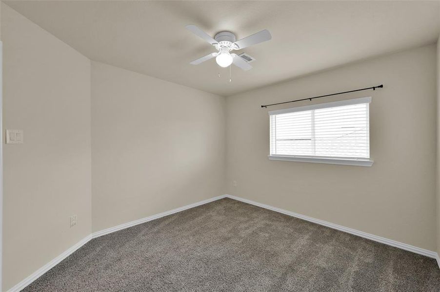 This is a well-lit, empty room featuring neutral walls, carpeted flooring, and a ceiling fan with a light fixture.