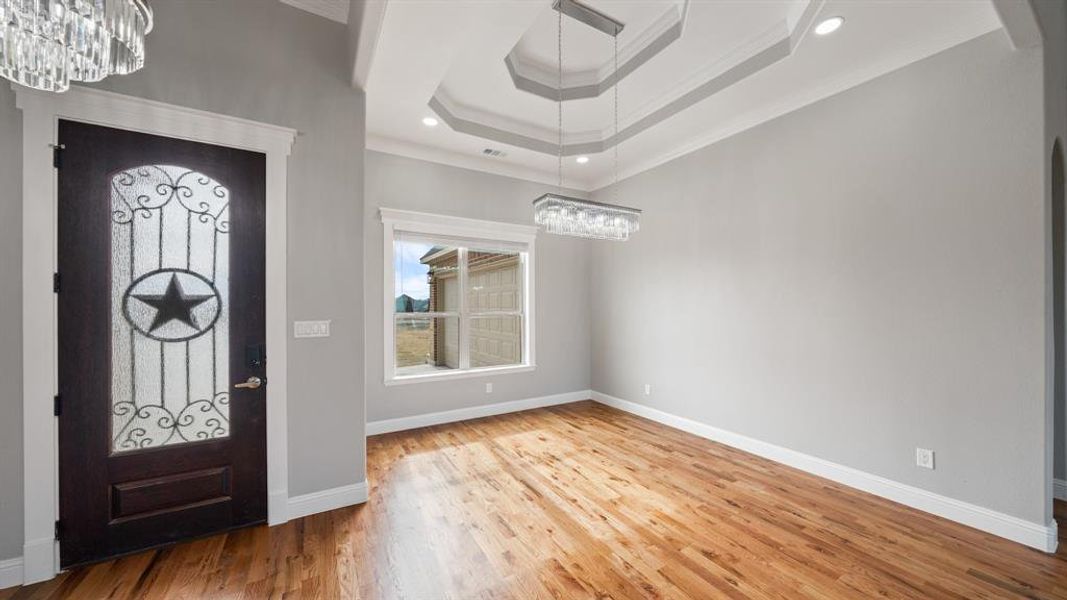 Foyer entrance featuring baseboards, ornamental molding, wood finished floors, an inviting chandelier, and a tray ceiling