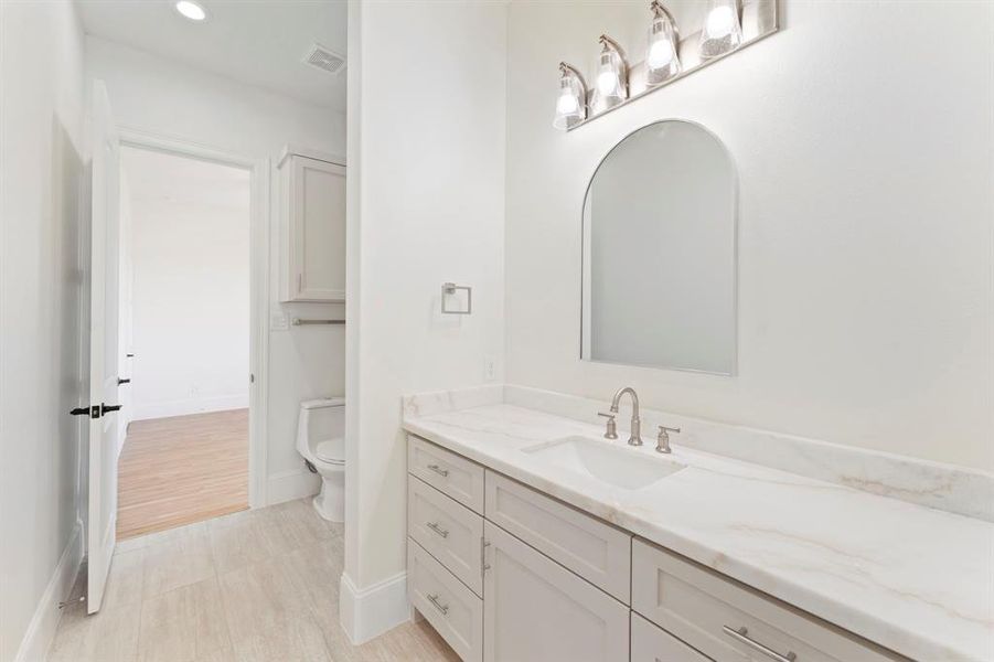 This is another bright bathroom featuring a large vanity with ample storage, Calacatta Lada marble countertop, an arched mirror, and overhead lighting.