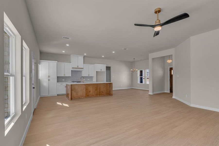 Kitchen with ceiling fan with notable chandelier, tasteful backsplash, white cabinetry, a large island with sink, and light hardwood / wood-style flooring