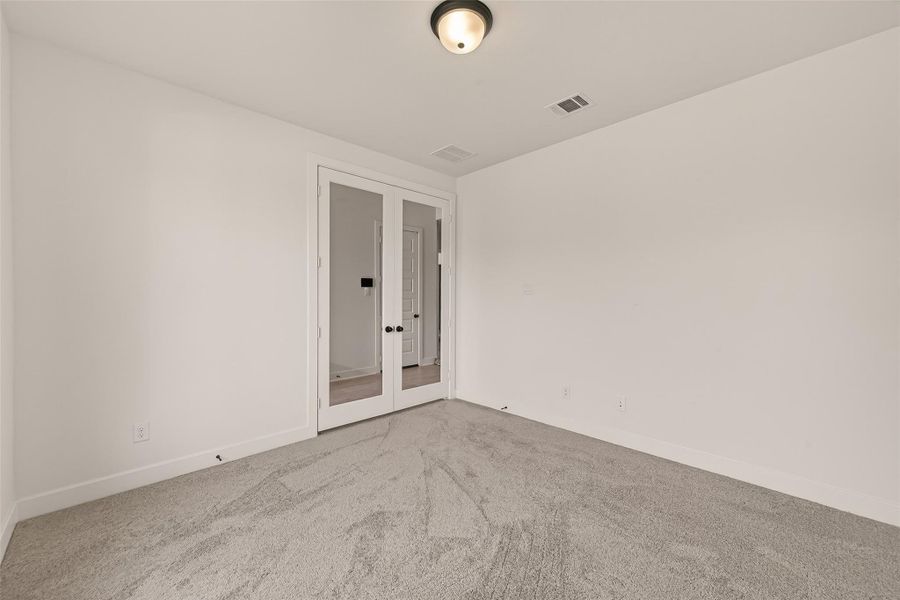 This home office features neutral carpeting, white walls, and double glass doors, providing a bright and versatile space perfect for an office or bedroom.