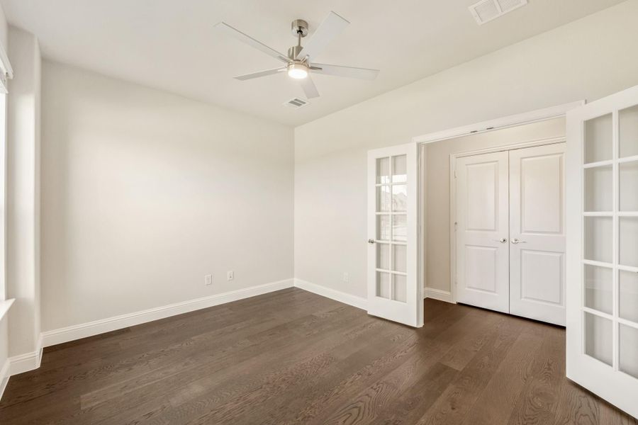 Empty bedroom with dark hardwood floors, ceiling fan, French doors, and double closet doors Empty bedroom with dark hardwood floors, ceiling fan, French doors, and double closet doors