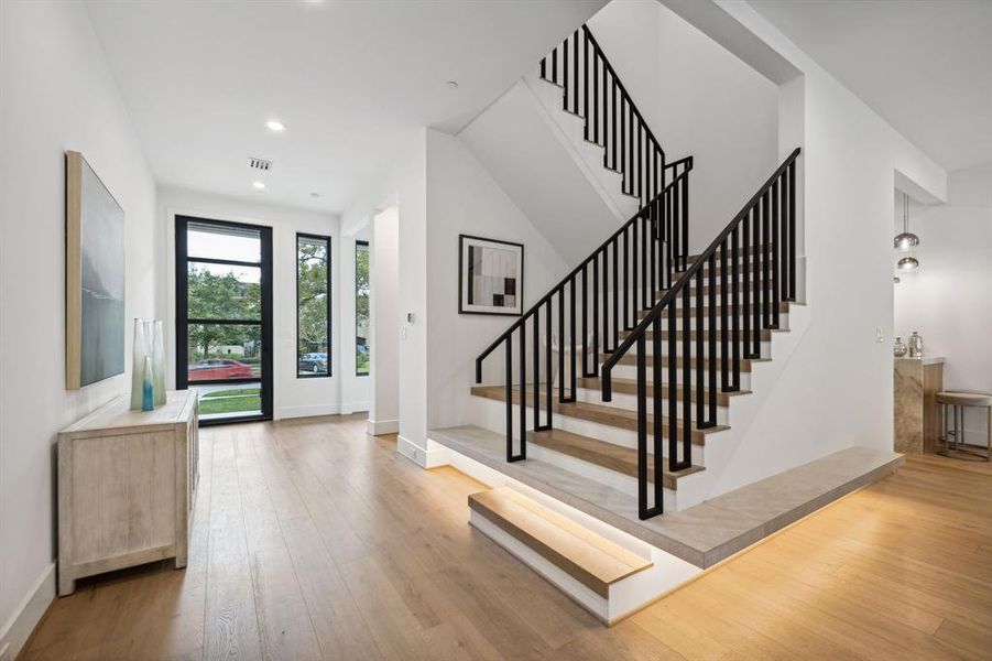 Continuing on from the entryway, you will find a sleek, modern staircase with black metal railings and warmwooden steps. It has a floating design with integrated LED lighting along the base.