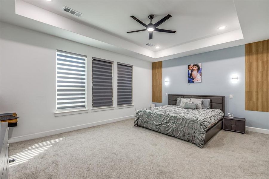 Spacious primary suite featuring a stylish accent wall, with plenty of room for a sitting area or home gym equipment. Enjoy a raised trey ceiling, luxury motorized blinds, a ceiling fan, and recessed lighting—creating a serene and sophisticated retreat! Spacious primary suite featuring a stylish accent wall, with plenty of room for a sitting area or home gym equipment. Enjoy a raised trey ceiling, luxury motorized blinds, a ceiling fan, and recessed lighting—creating a serene and sophisticated retreat!