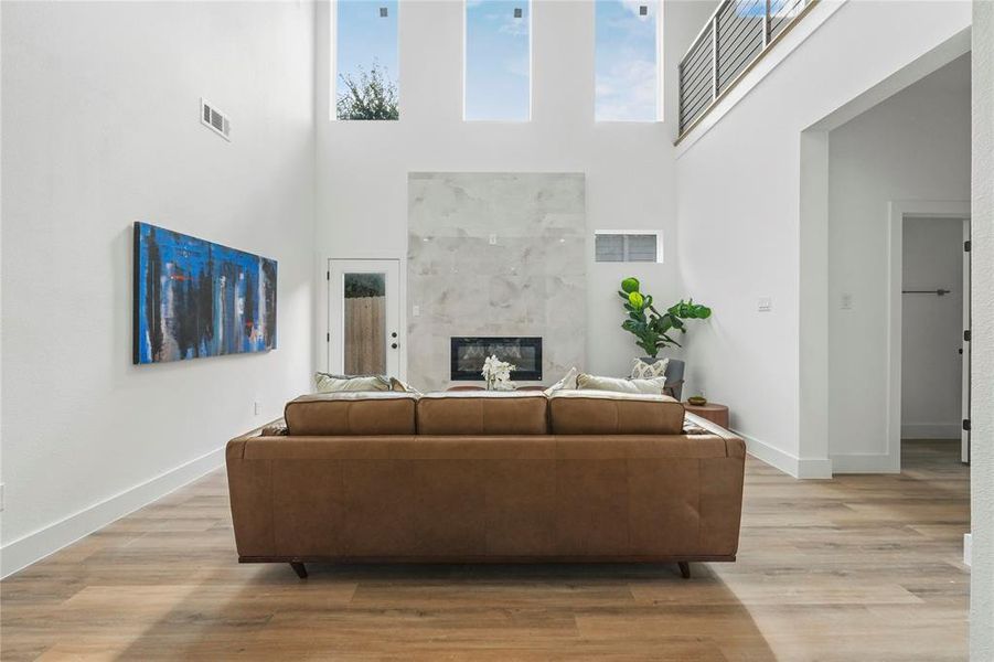 Living room with a fireplace, a high ceiling, light wood-type flooring, and healthy amount of natural light