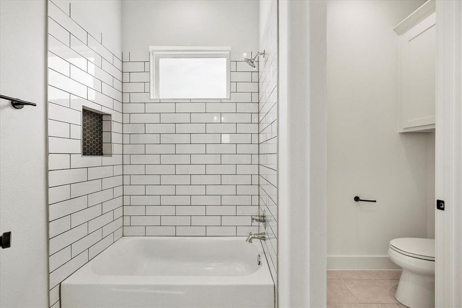 Bathroom featuring tiled shower / bath, toilet, and tile patterned flooring