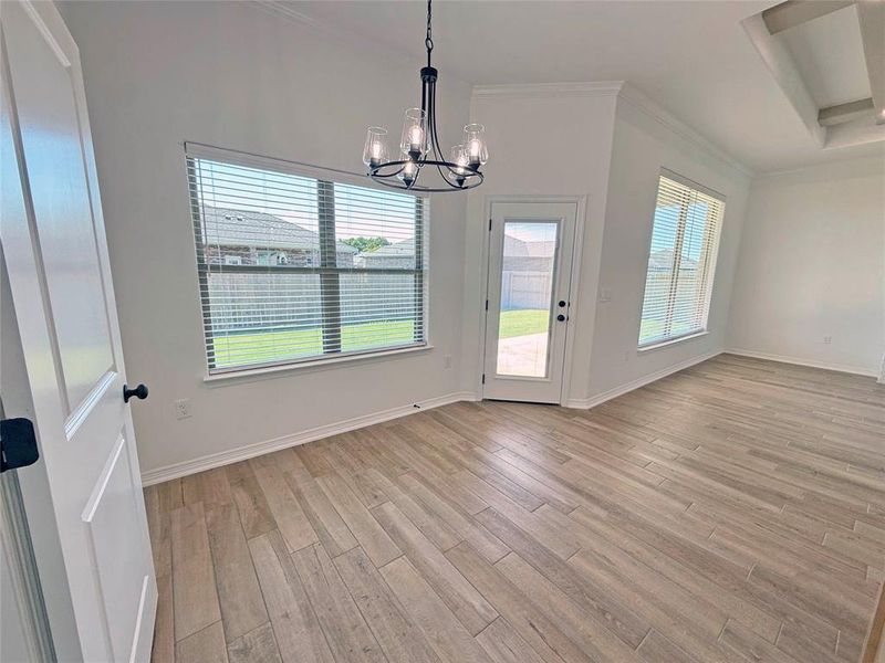 Unfurnished dining area with healthy amount of natural light, a chandelier, light wood-style floors, and crown molding