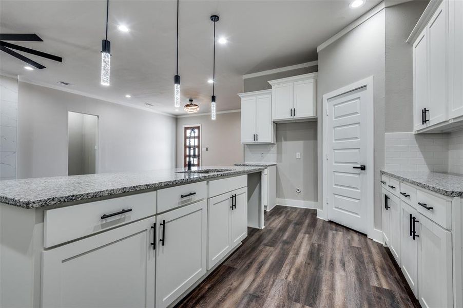 Kitchen with crown molding, dark wood-style flooring, a ceiling fan, decorative backsplash, and light stone counters Kitchen with crown molding, dark wood-style flooring, a ceiling fan, decorative backsplash, and light stone counters