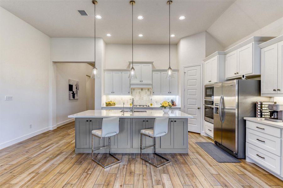 Kitchen featuring a breakfast bar area, pendant lighting, a center island with sink, stainless steel appliances, and decorative backsplash