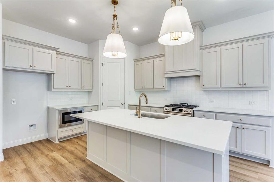 Kitchen with pendant lighting, light wood-type flooring, stainless steel appliances, and sink