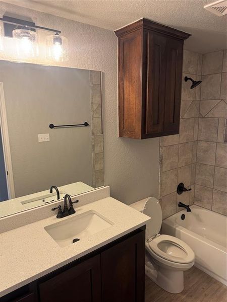 Full bathroom with wood-type flooring, toilet, a textured ceiling, and tiled shower / bath combo