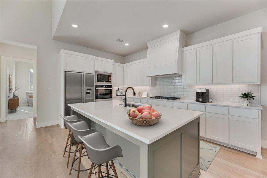 Kitchen with white cabinets, light wood-style floors, decorative backsplash, stainless steel appliances, and a kitchen island with sink Kitchen with white cabinets, light wood-style floors, decorative backsplash, stainless steel appliances, and a kitchen island with sink