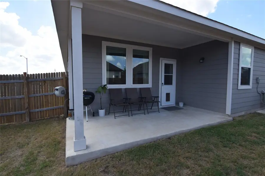 A covered concrete patio provides shelter alongside a wooden fence and level lawn.