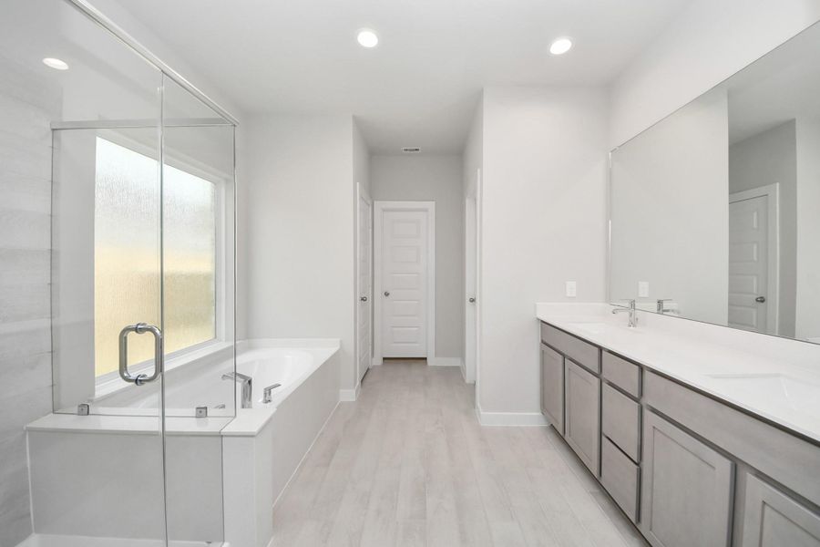 Escape to a spa-like oasis in this primary bathroom. Enjoy a walk-in shower with tile surround, a separate garden tub with custom detailing, and an elegant vanity featuring light countertops, modern hardware, and beautiful recessed lights. Experience luxury and relaxation in every detail! Sample photo of completed home with similar floor plan. Actual colors and selections may vary.