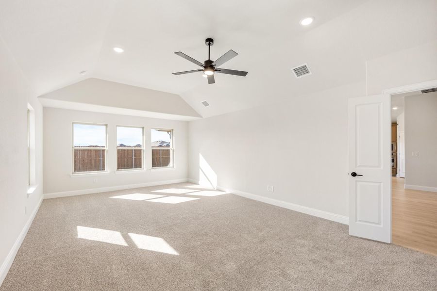 Empty bedroom with vaulted ceiling, ceiling fan, carpet flooring, and three windows