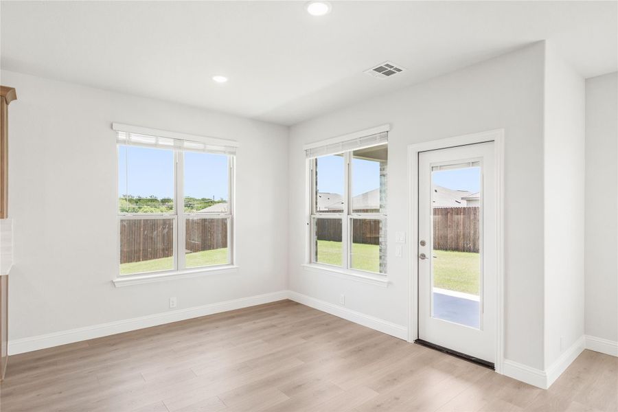 Bright empty room with light wood floors, two windows, and a glass back door overlooking a fenced yard