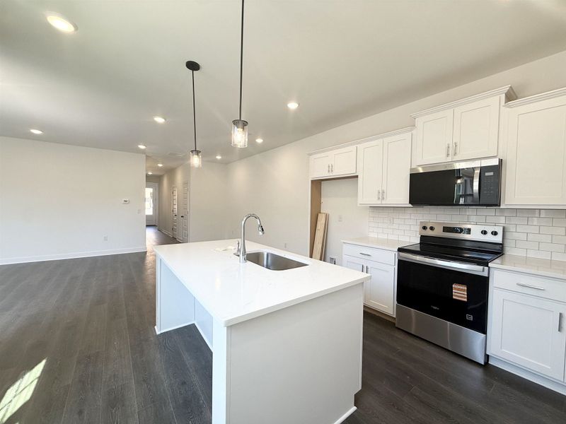 Kitchen with stainless steel appliances, white cabinets, an island with sink, and light stone countertops