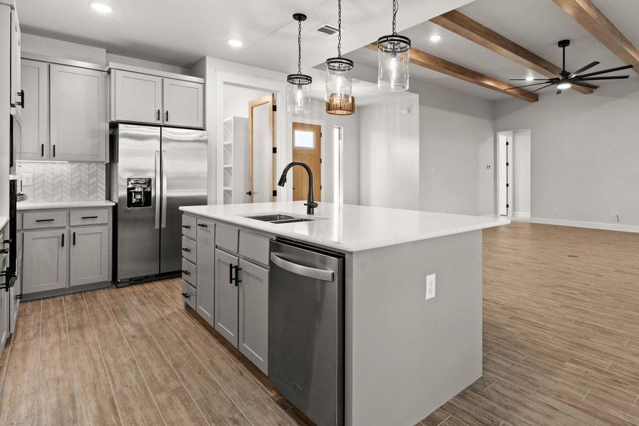 Kitchen featuring a kitchen island with sink, appliances with stainless steel finishes, hanging light fixtures, gray cabinets, and beam ceiling Kitchen featuring a kitchen island with sink, appliances with stainless steel finishes, hanging light fixtures, gray cabinets, and beam ceiling