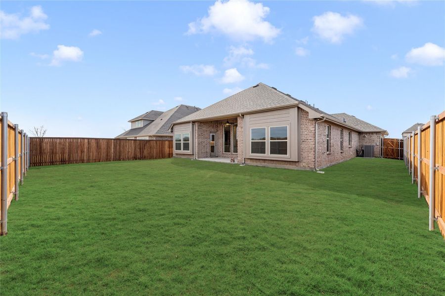 Brick home rear exterior with large fenced backyard and green lawn Brick home rear exterior with large fenced backyard and green lawn