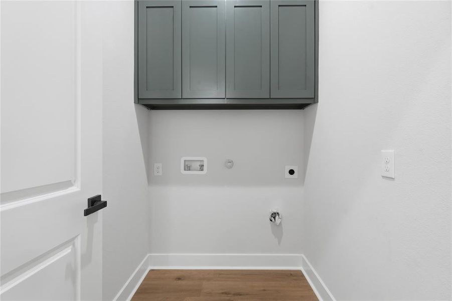 Dedicated utility space featuring wood-finish flooring, white baseboards, and built-in upper cabinetry with a dark finish Dedicated utility space featuring wood-finish flooring, white baseboards, and built-in upper cabinetry with a dark finish