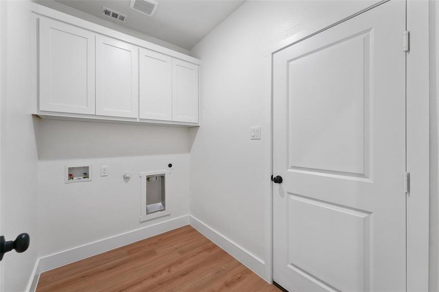 Laundry area featuring wood-finish flooring, white shaker-style cabinetry, and crisp white walls Laundry area featuring wood-finish flooring, white shaker-style cabinetry, and crisp white walls