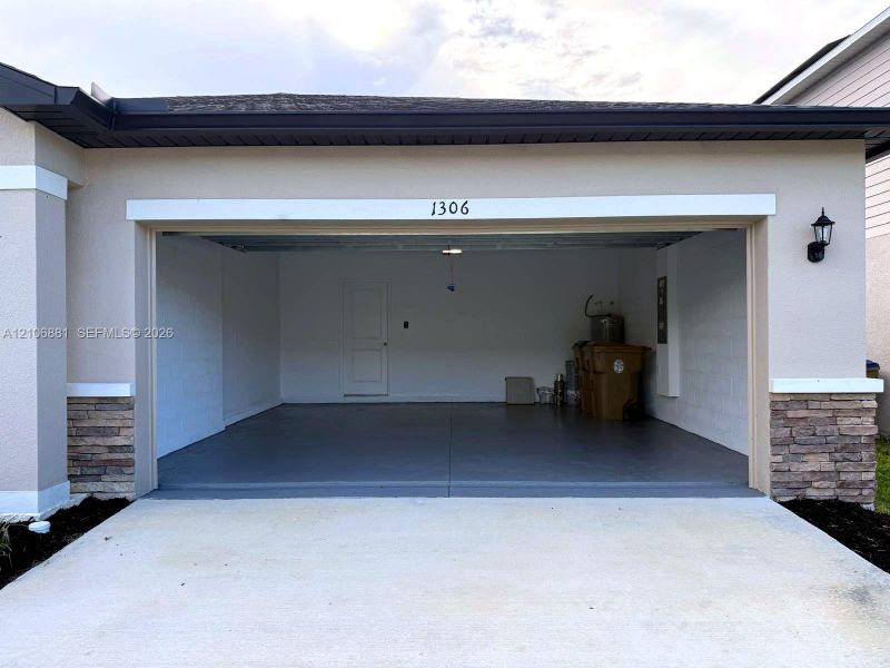 Two-car garage featuring finished concrete flooring, exterior stone veneer accents, and an attached wall-mounted lantern light