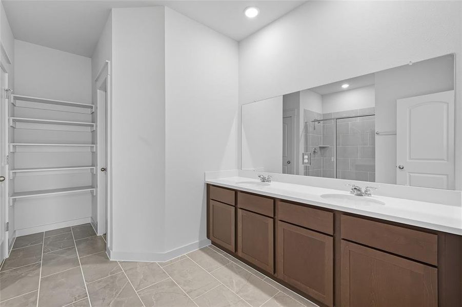 Full bath featuring a walk in closet, a shower stall, double vanity, and light tile patterned floors Full bath featuring a walk in closet, a shower stall, double vanity, and light tile patterned floors