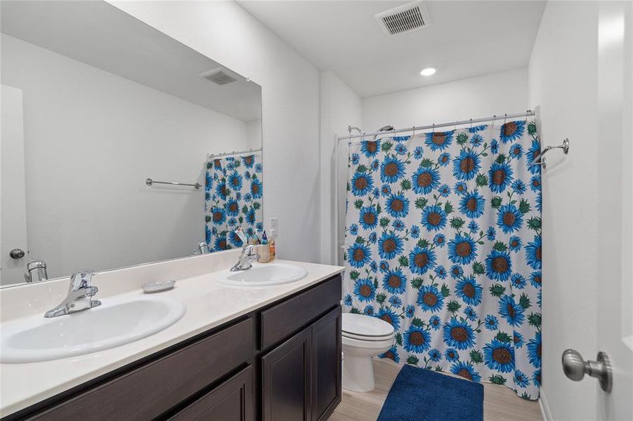 Full bath with double vanity, light wood-type flooring, and a shower with shower curtain
