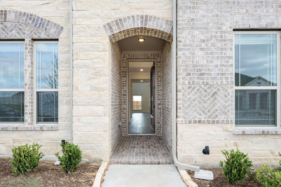 Home entrance with arched brick doorway, stone and brick exterior, and open front door
